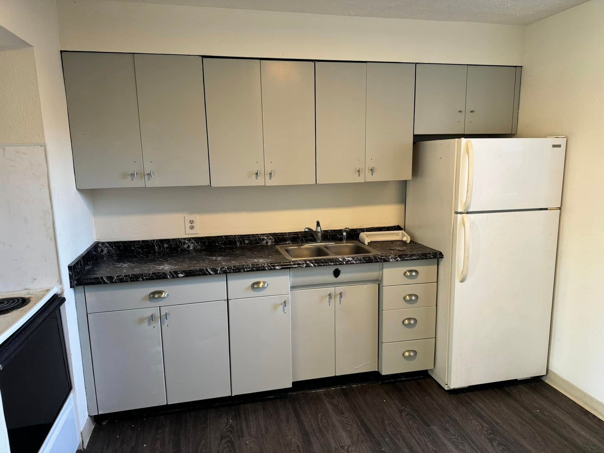 Kitchen with gray cabinets, black countertop, stainless steel sink, and white refrigerator.