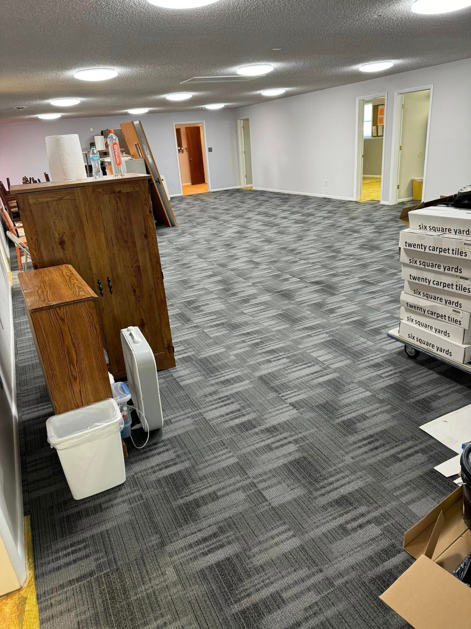 Empty room with gray carpet, white walls, overhead lights, and wooden furniture. Doors visible.