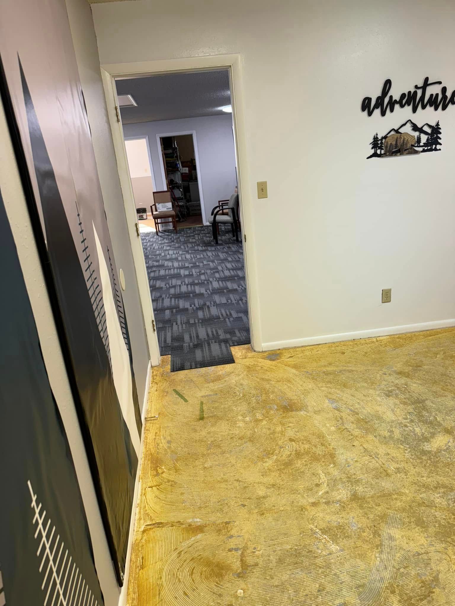 View of an office space with ripped-up, yellow floor tiles, open doorway to another office, and an 