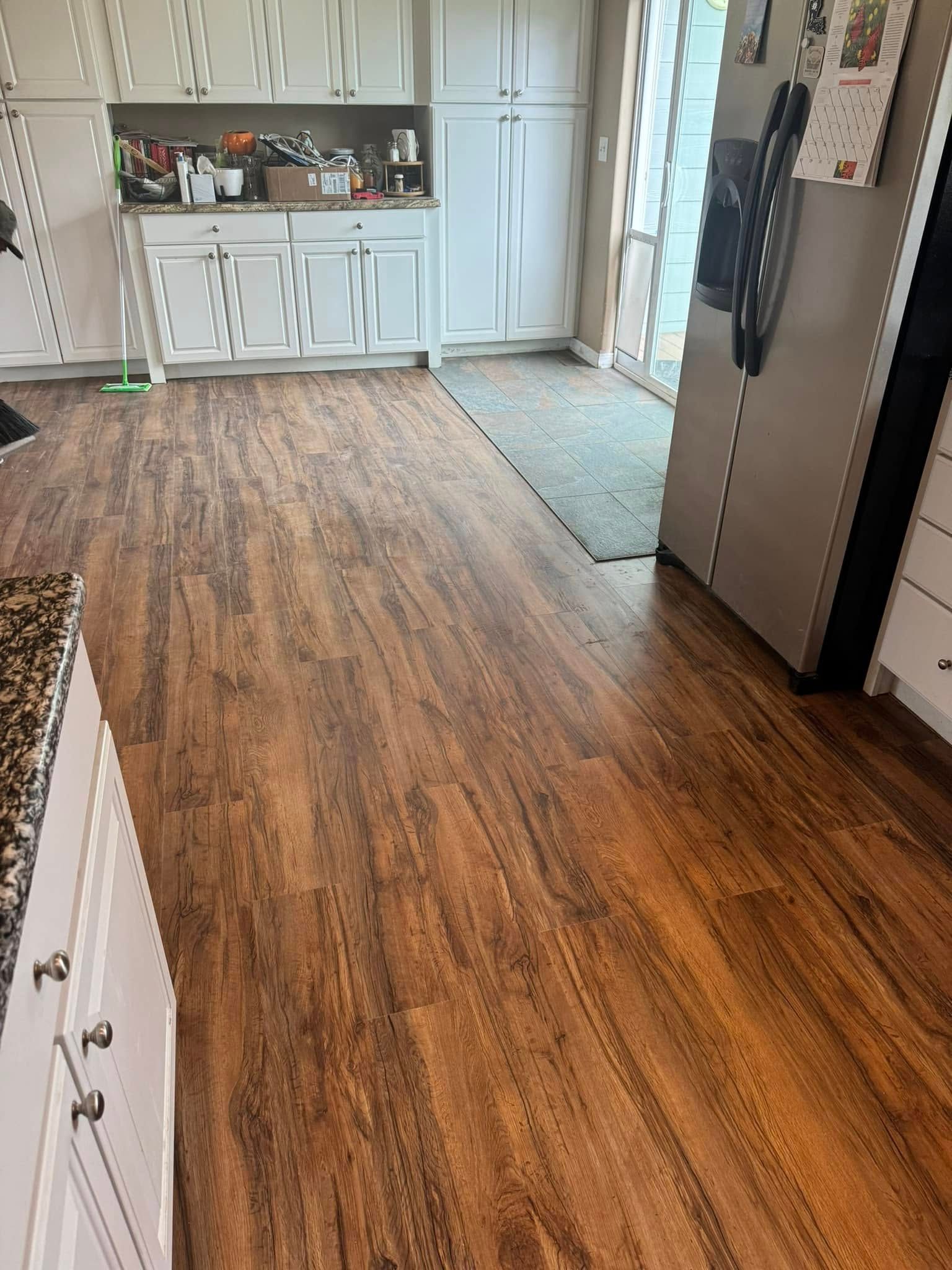 Wooden floor in a kitchen with white cabinets, a refrigerator, and a sliding glass door.