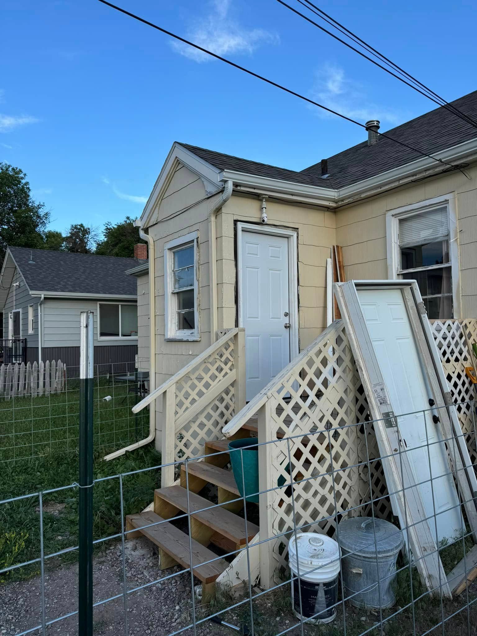 Back entrance of a beige house with latticework, steps, and a partially open white door.