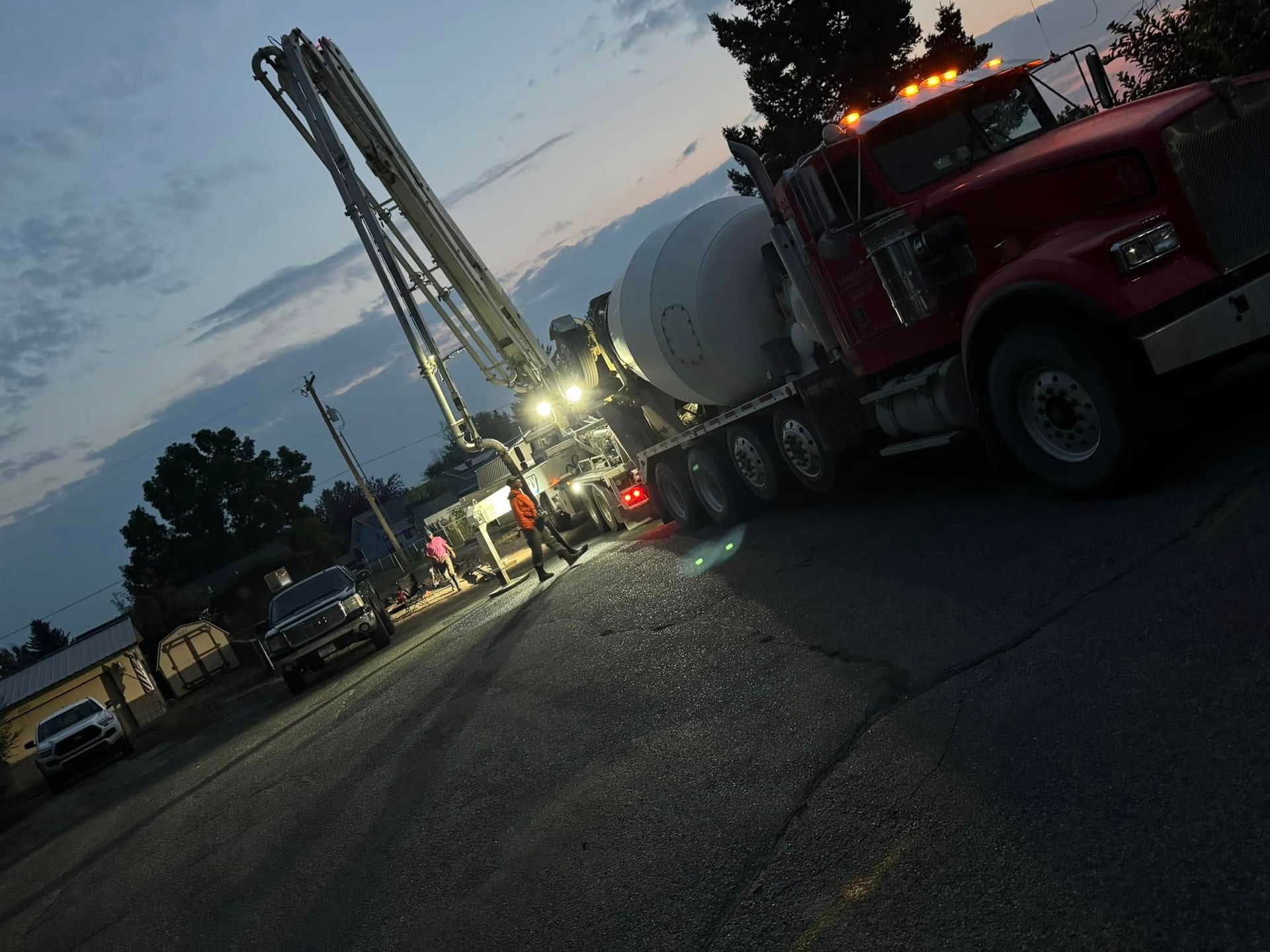 Red cement truck pouring concrete at dusk, crew present.