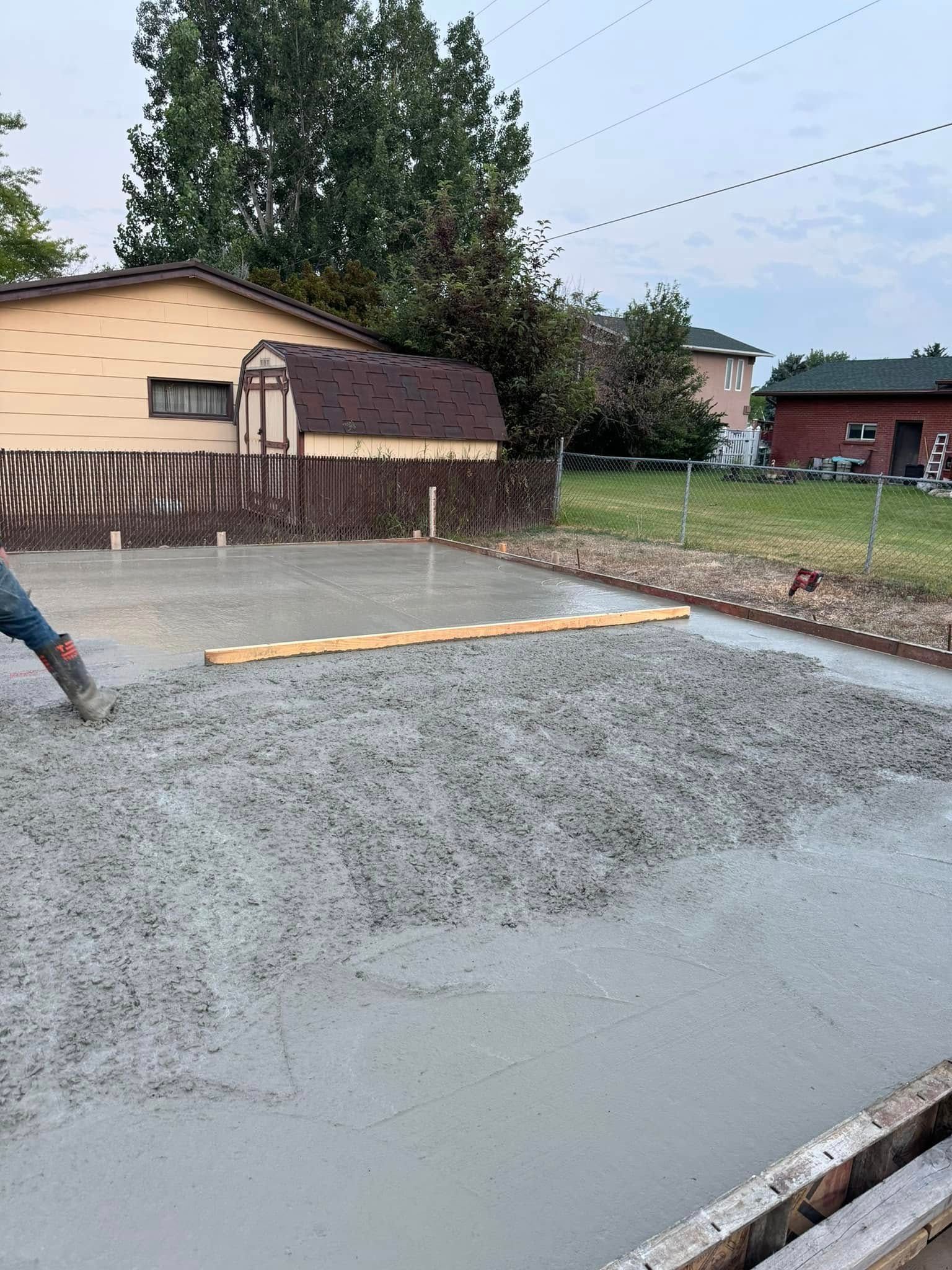 Freshly poured concrete being leveled, with wooden forms, in a backyard setting.