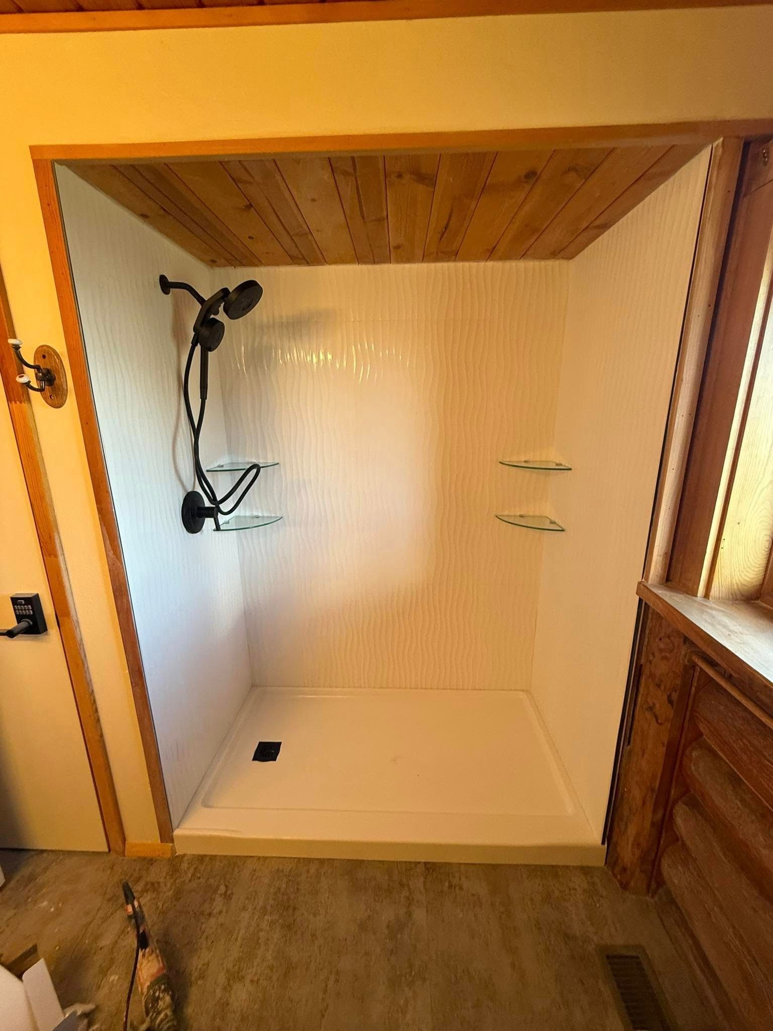 White shower stall with black fixtures and glass shelves, wood trim.