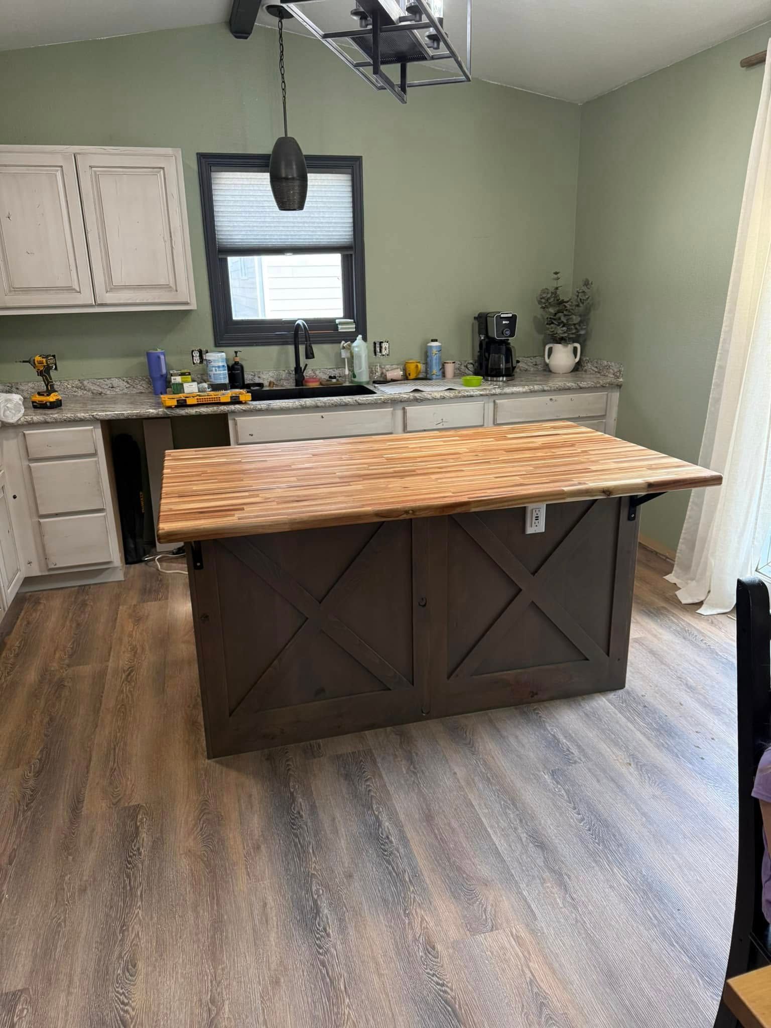 Kitchen with dark brown island, light wood countertop, white cabinets, and sage green walls.