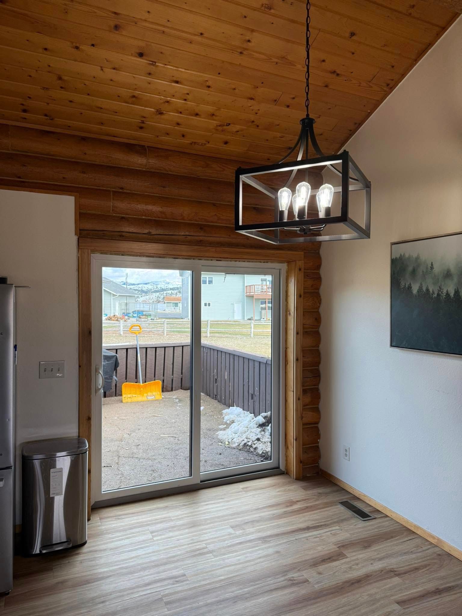 Dining room with sliding glass door, wood ceiling and floors, and a modern chandelier.