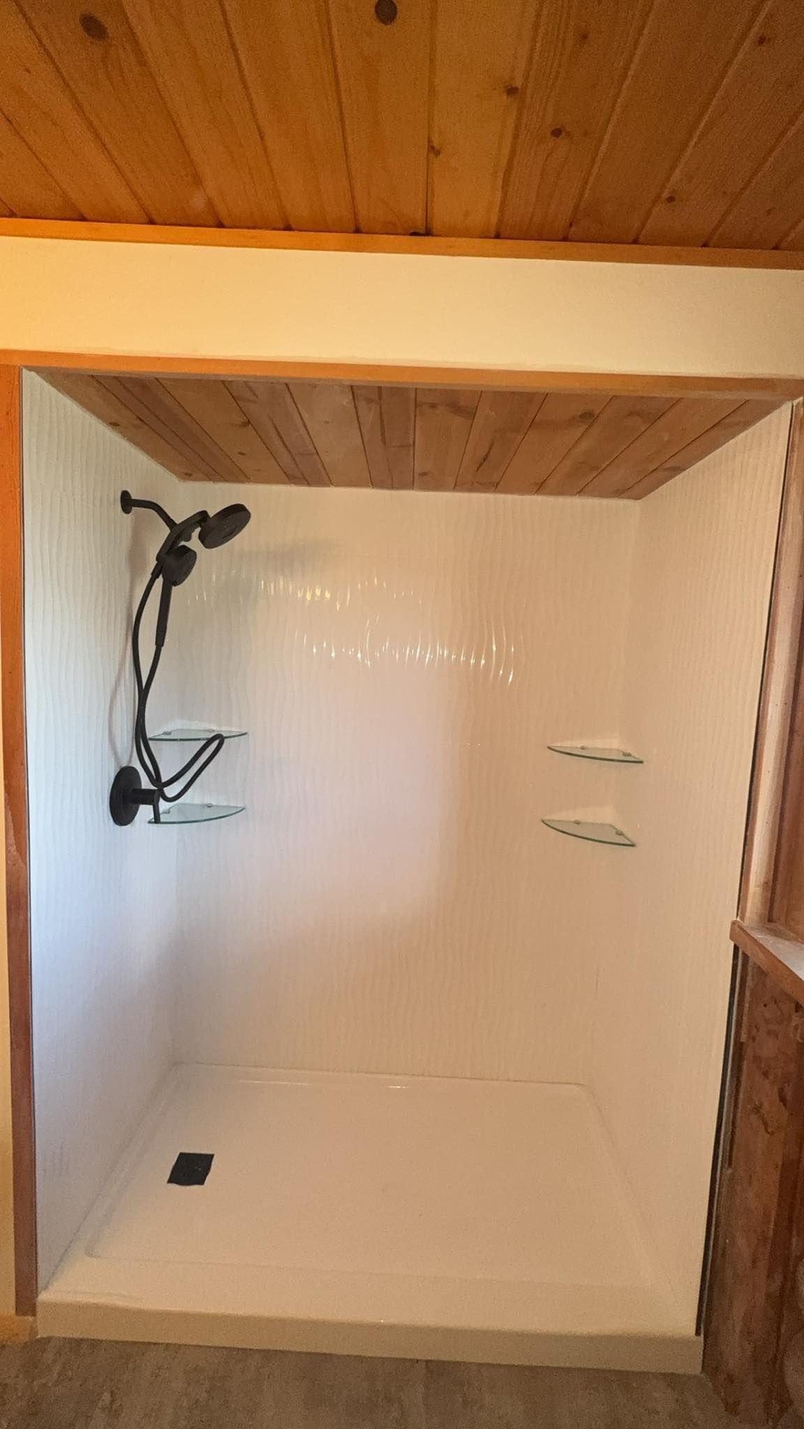 White-walled shower with black fixtures and a wooden ceiling.