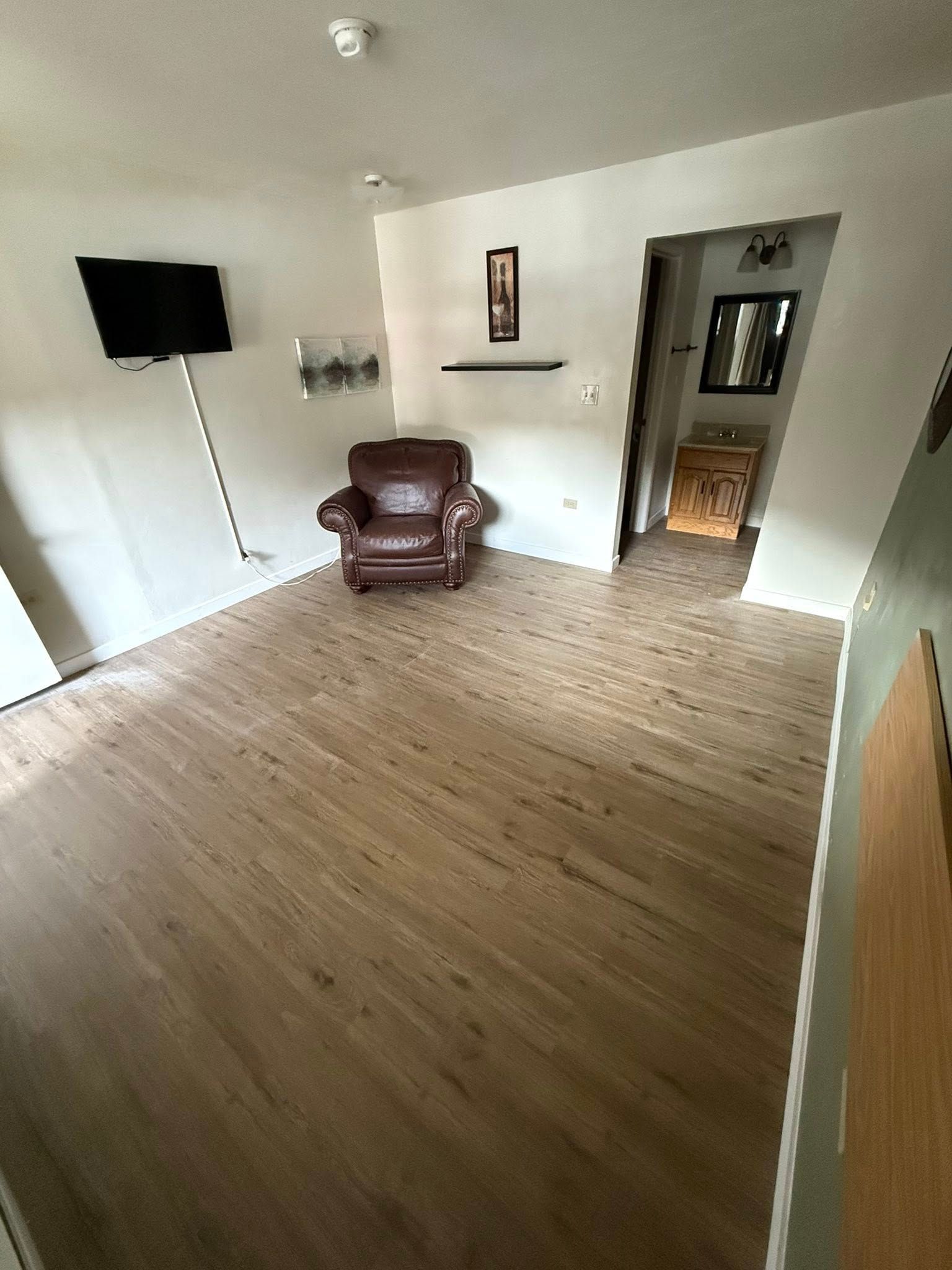 Living room with wooden floors, brown leather armchair, and mounted TV.