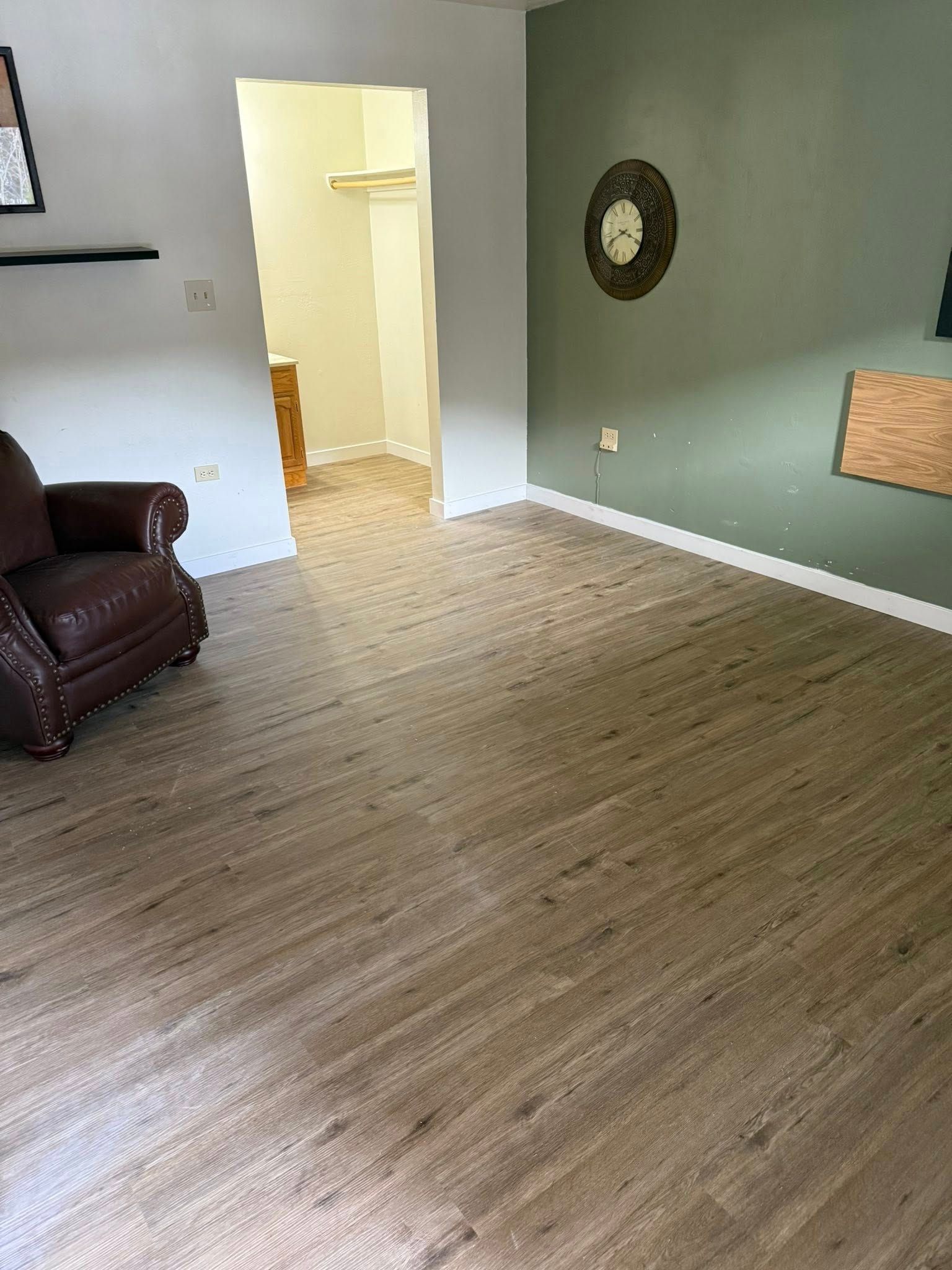 Living room with brown flooring, an armchair, and an open doorway to another room. Olive green wall.