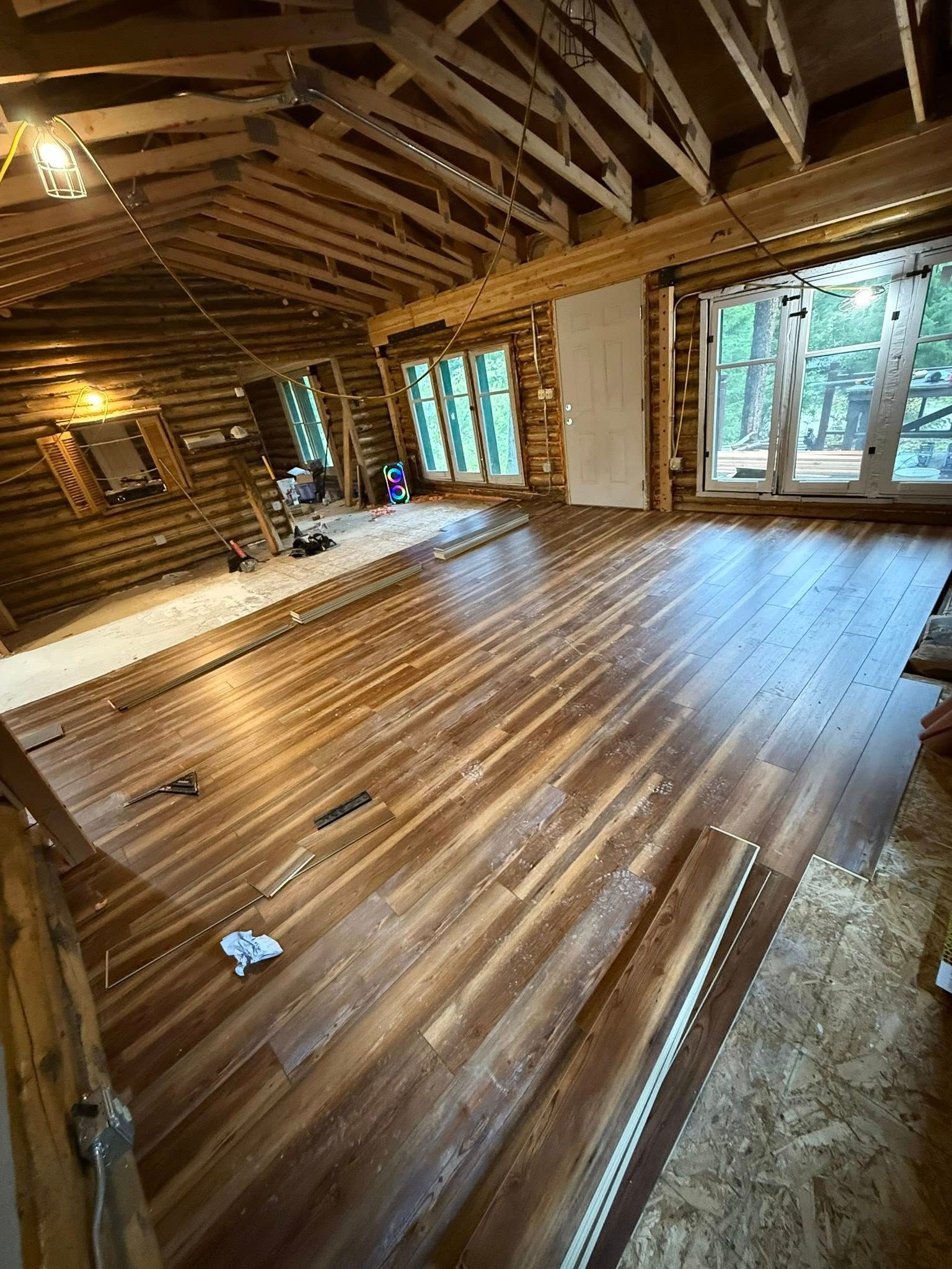 Interior room with wood flooring, log walls, and windows.