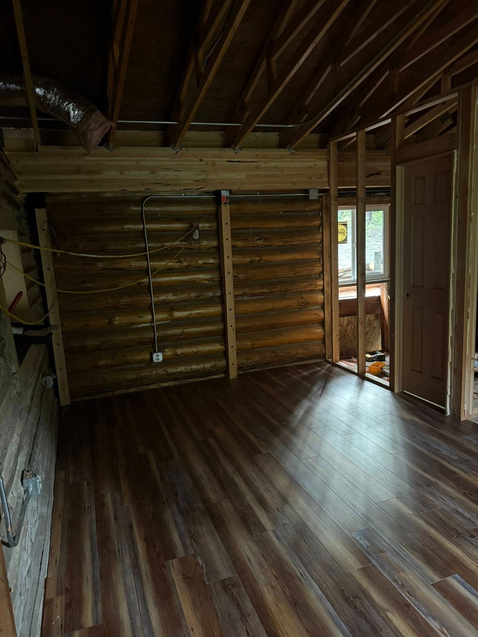 Interior of a room under construction, with wood panel walls, a wood floor, and exposed ceiling beams.