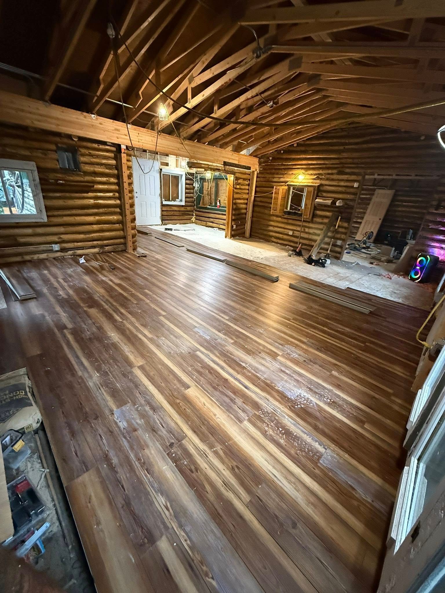 Interior of a rustic log cabin with new hardwood floors, open beams, and a visible doorway.