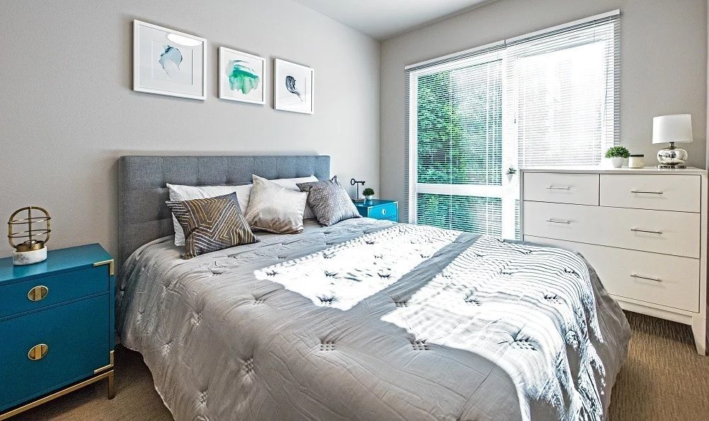 Bedroom with gray bed, blue nightstands, white dresser, sliding glass door, and art prints on the wall.