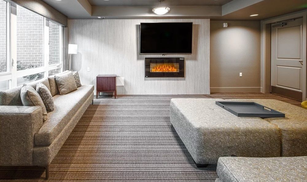 A modern living room with a gray sofa, large ottoman, fireplace, and mounted TV.