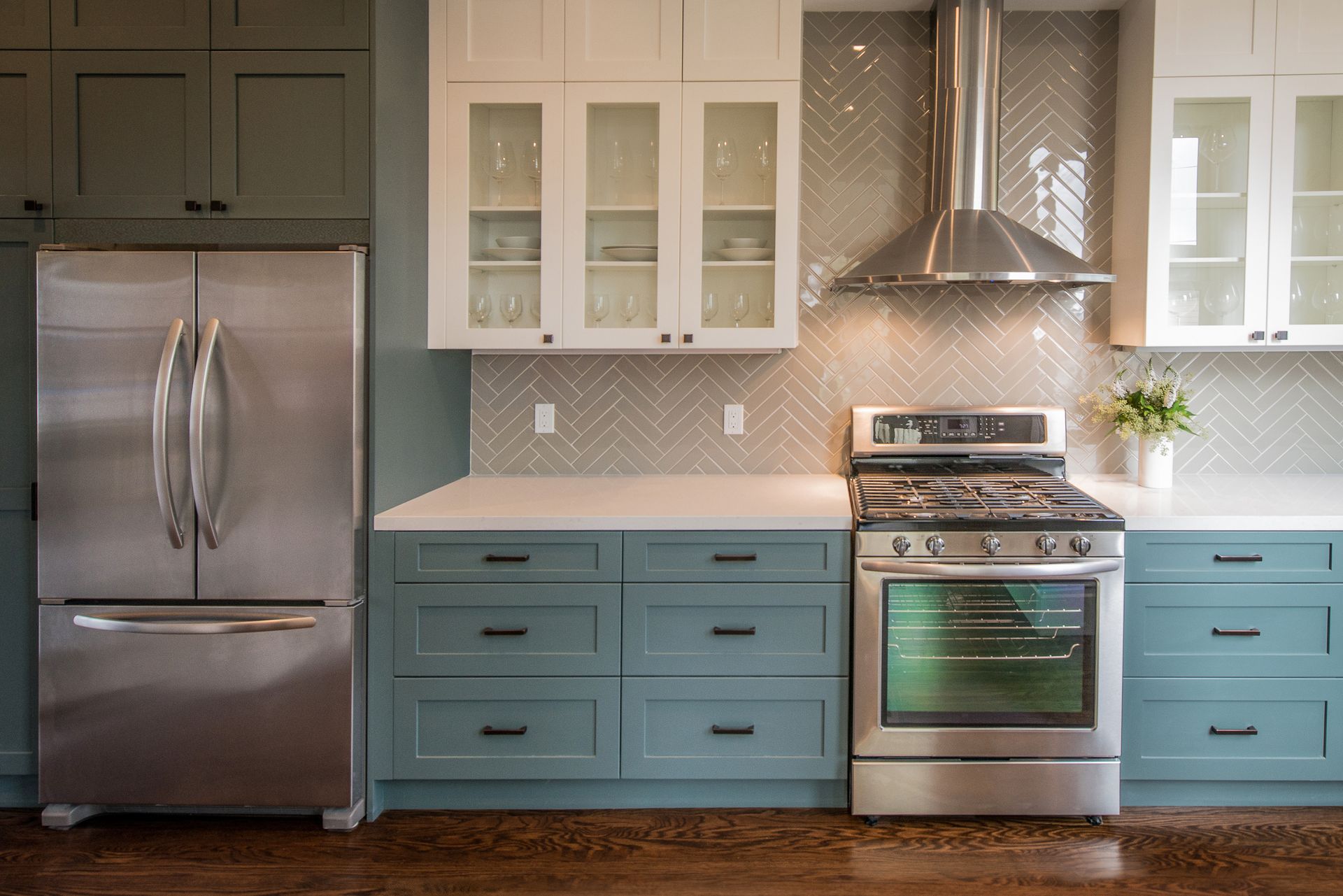 Modern kitchen with stainless steel appliances, blue cabinets, white upper cabinets, and a herringbone backsplash