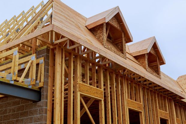 Wood-frame house under construction with exposed timber framing and roof trusses