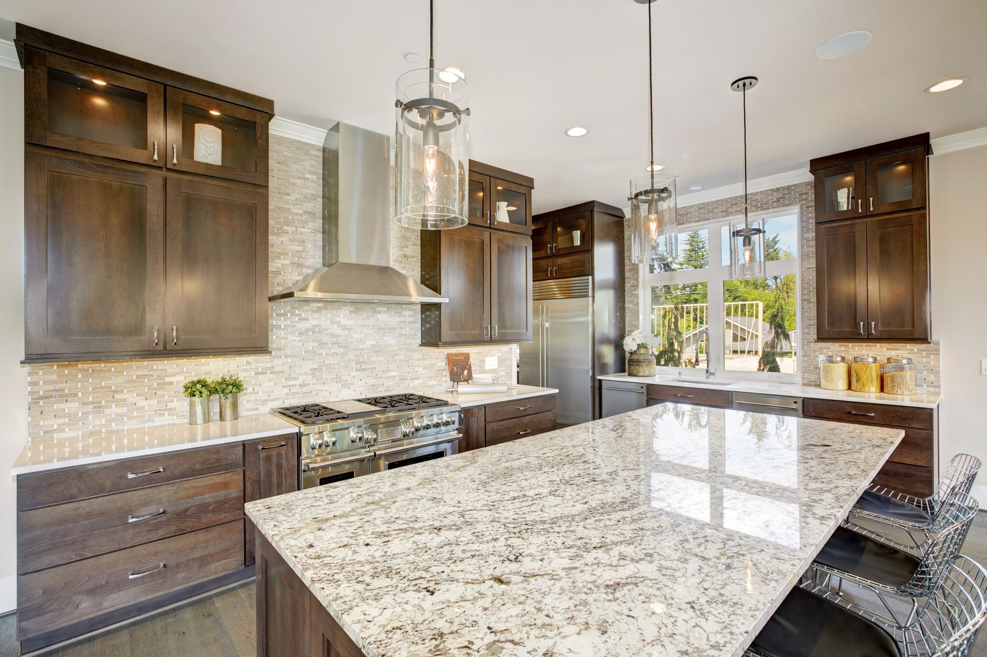 Modern kitchen with dark wood cabinets, granite island, stainless hood, and large windows