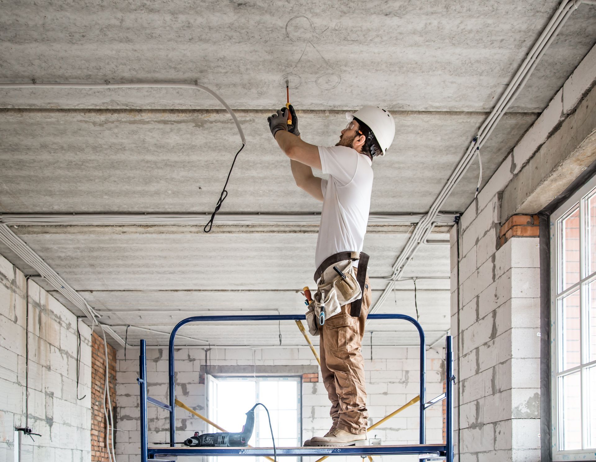 Worker drilling into a concrete ceiling from a scaffold inside an unfinished building