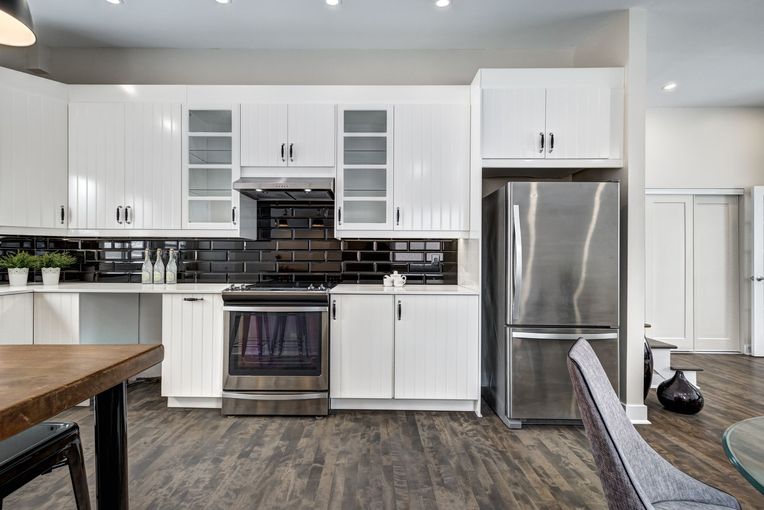 Bright modern kitchen with white cabinets, stainless steel appliances, and dark wood flooring