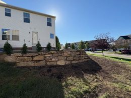 White house with stone retaining wall and small trees in a sunny suburban yard