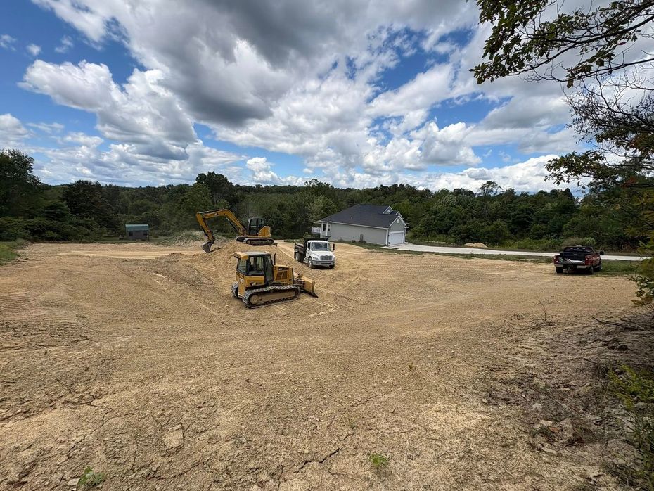 Construction site with excavators and trucks on a dirt lot under a cloudy sky