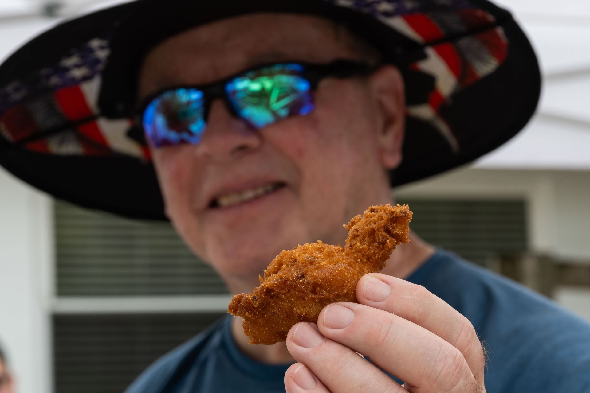 Man in patriotic hat and sunglasses holding a piece of fried food.