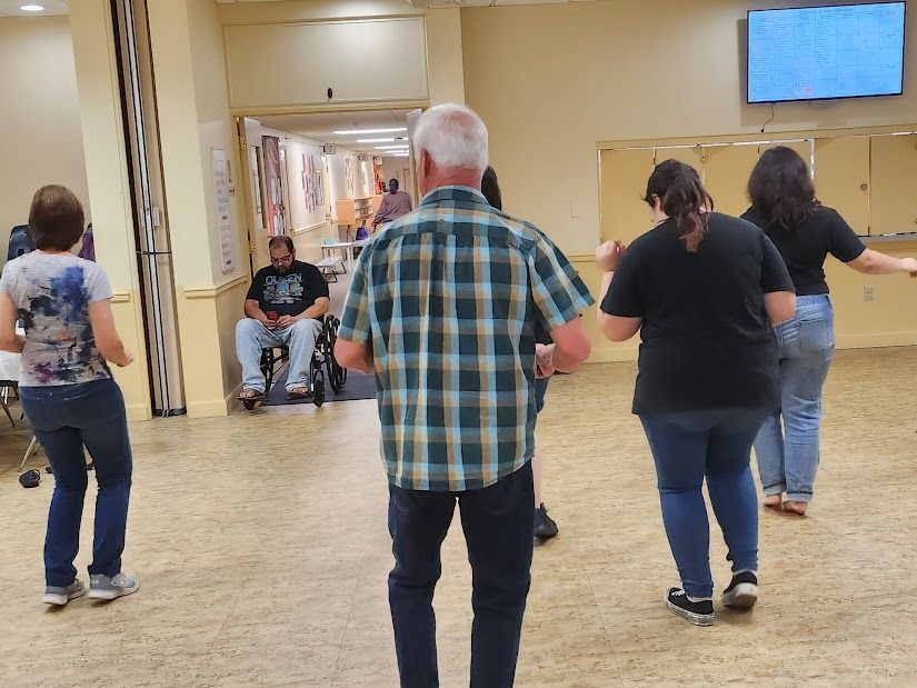 People dancing in a community hall. One person in a wheelchair watches.