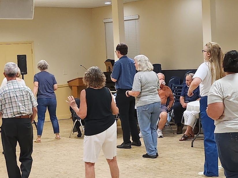 People dancing in a room. Some are in jeans, a man in a blue shirt is in the middle.