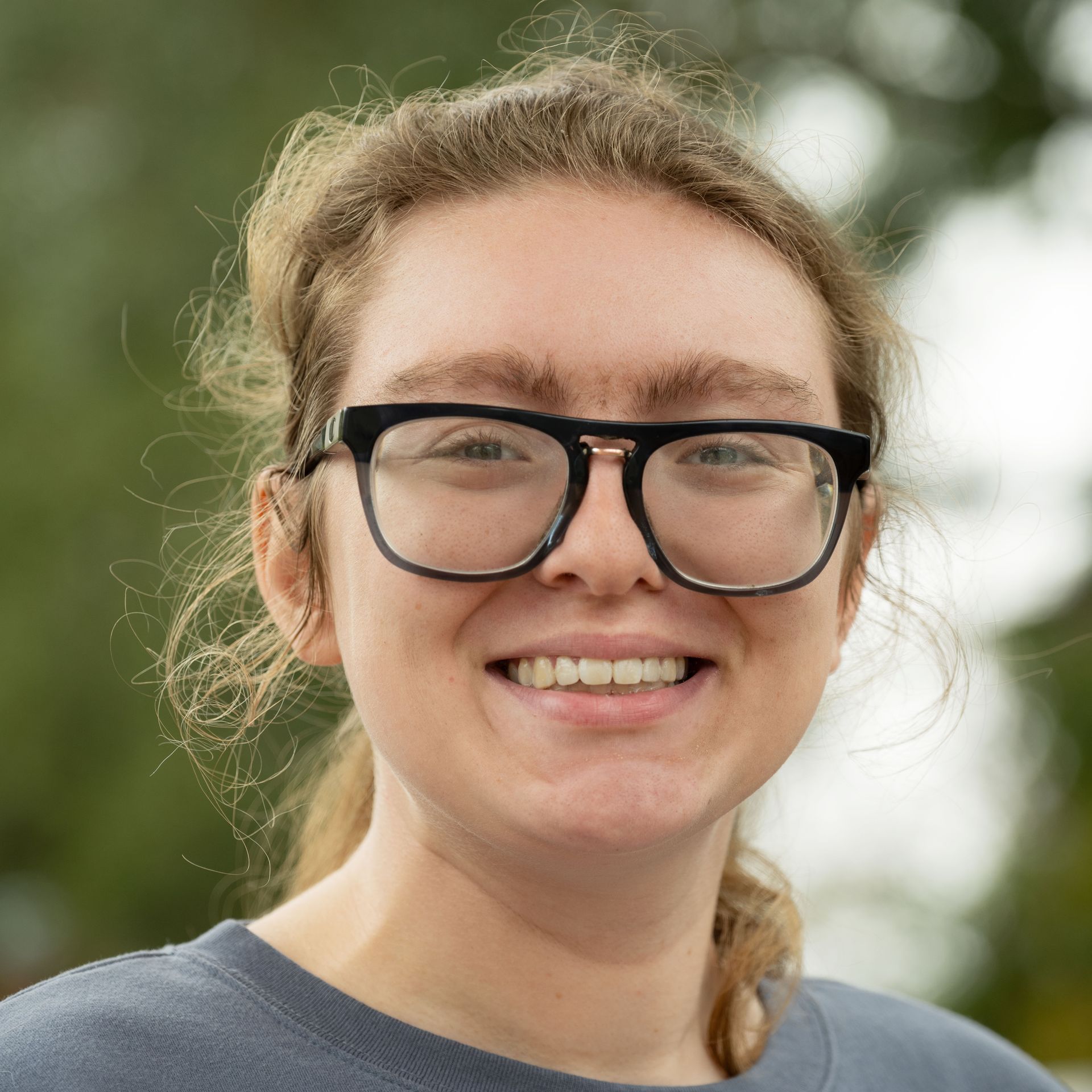 Woman with glasses smiles, looking directly at the camera.