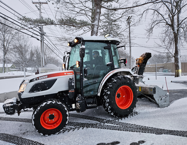 A tractor is plowing snow in a parking lot