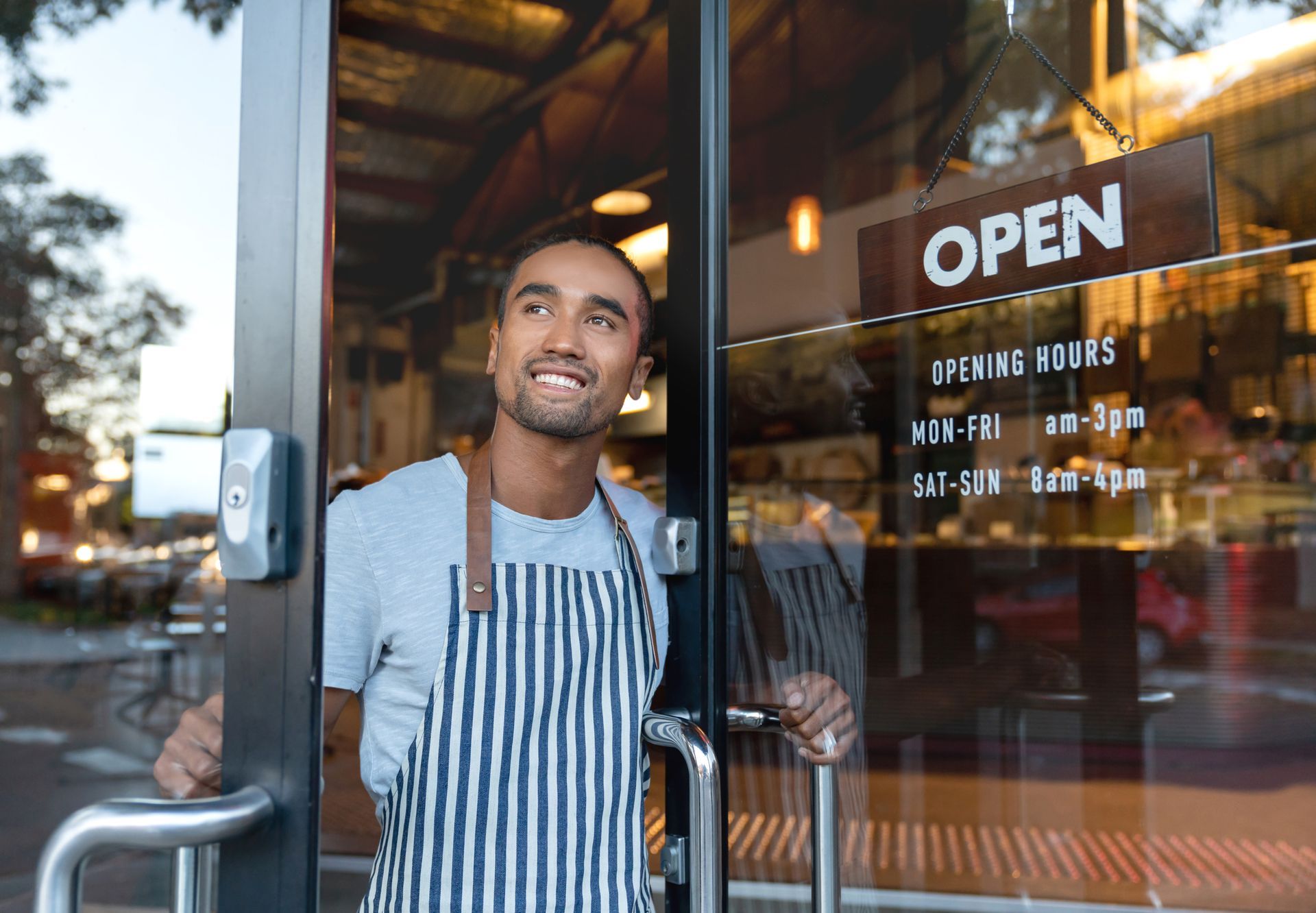 A man in an apron is standing in the doorway of a restaurant.