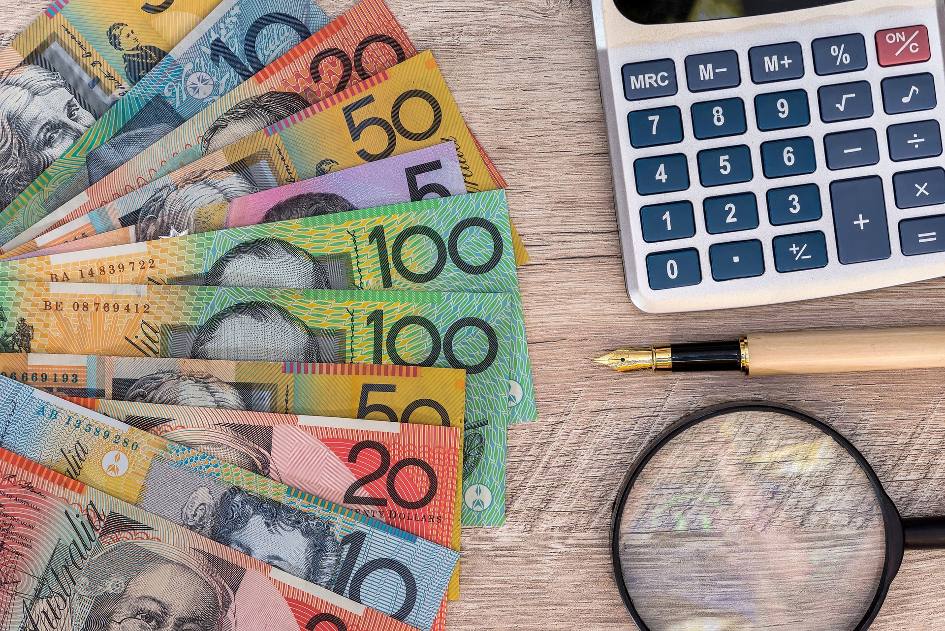 A bunch of money is sitting on a table next to a magnifying glass and a calculator.