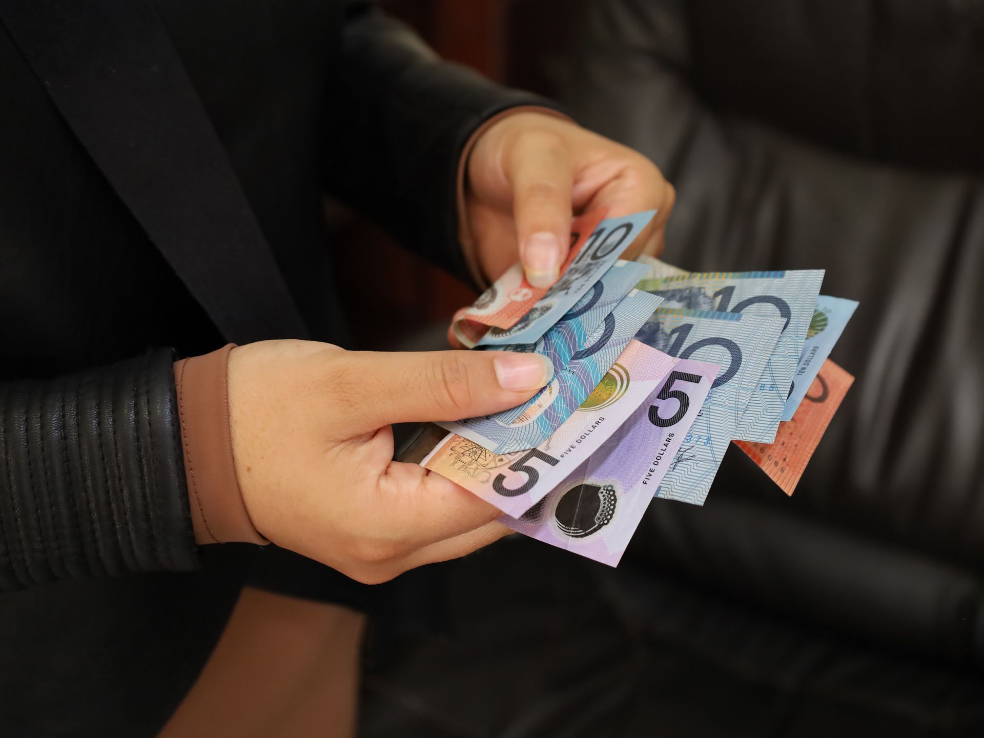 A person is holding a bunch of australian money in their hands