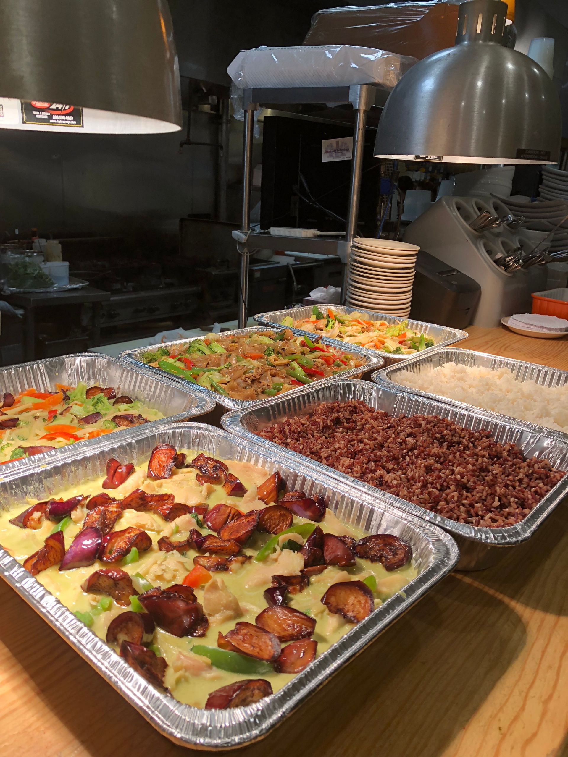 A variety of Chinese food dishes in foil pans, set on a counter under heat lamps.