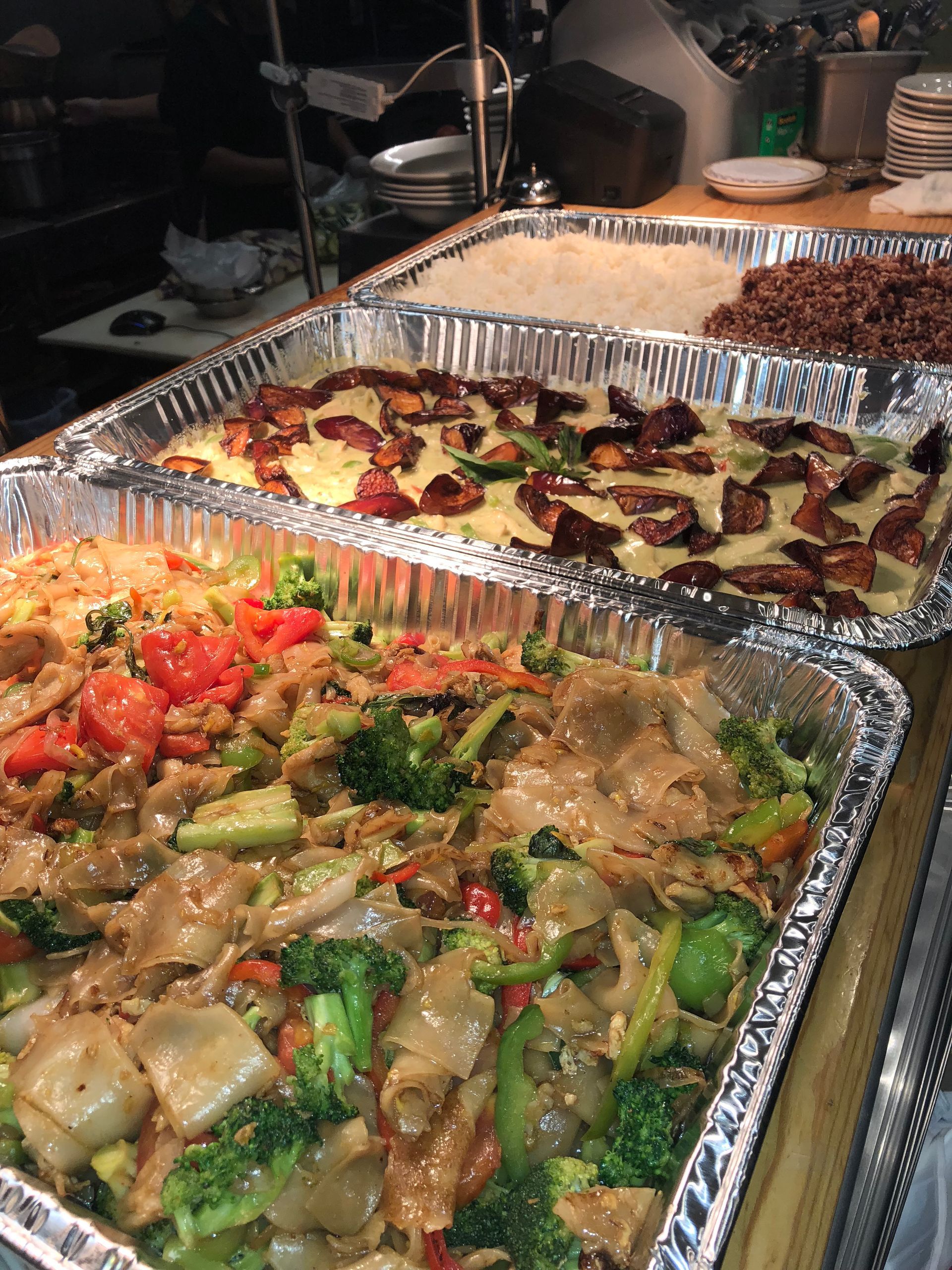 Trays of prepared food: Pad See Ew with broccoli, baked dish with bacon, and grains.