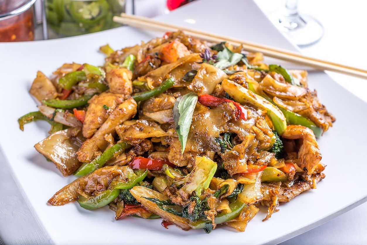 Pad See Ew noodles with vegetables and chicken on a white plate with chopsticks.