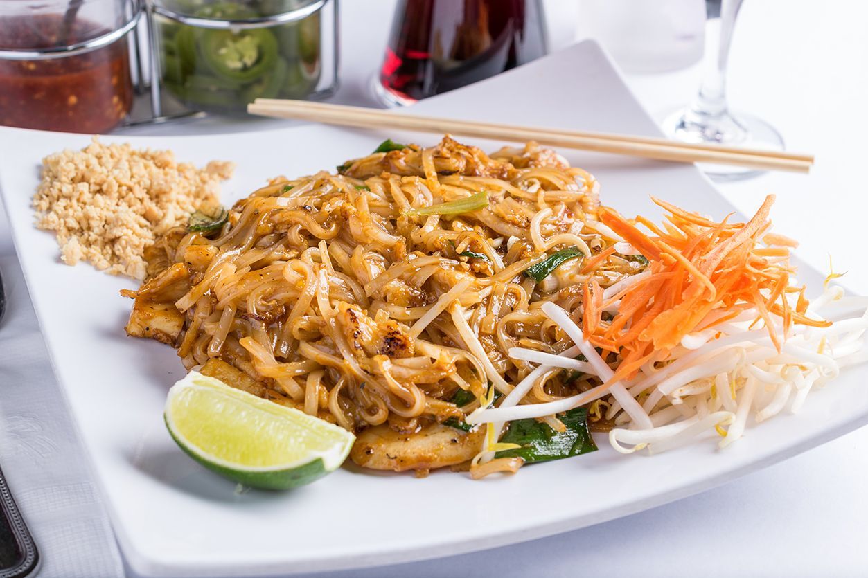Pad Thai dish on a white plate with peanuts, lime, and carrots.