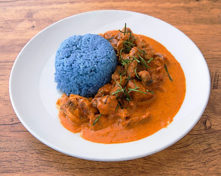 Plate of red curry beef with blue rice on a wooden table.