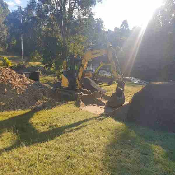 A yellow excavator is digging a hole in a grassy field.