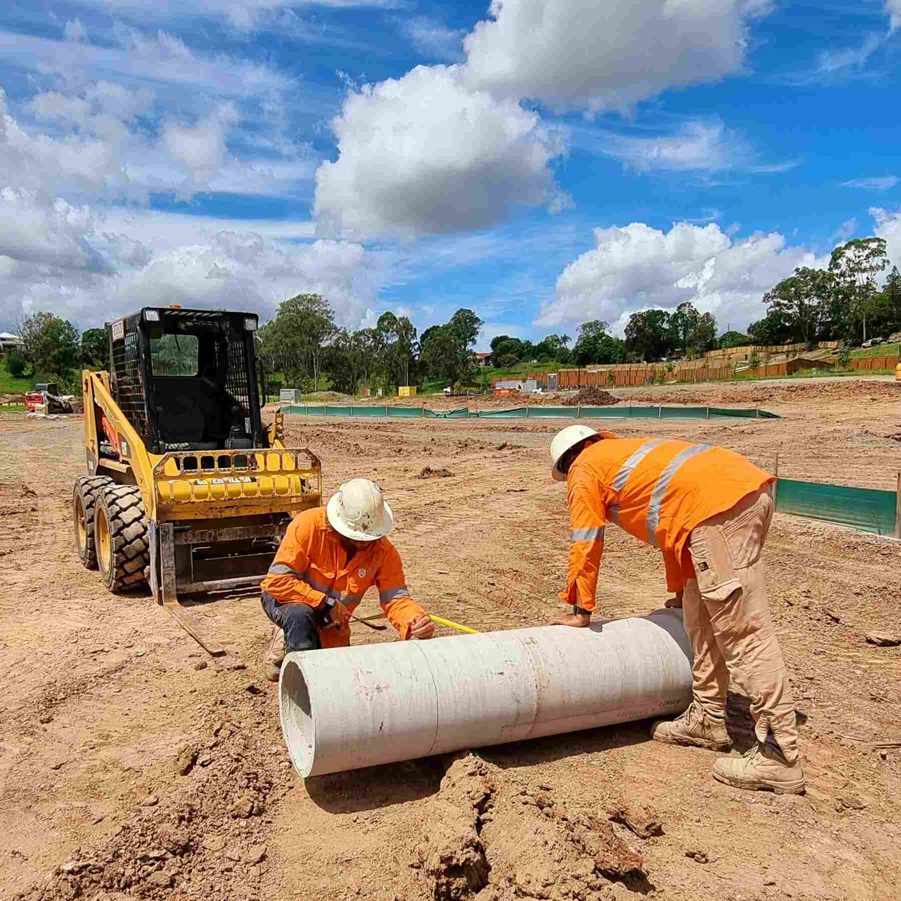 Two construction workers are working on a large pipe in the dirt.