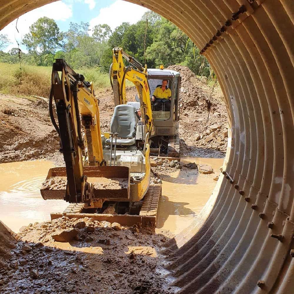 A yellow excavator is driving through a muddy tunnel.