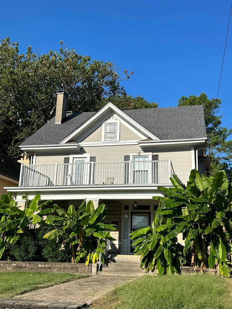 A large house with a balcony and banana trees in front of it.
