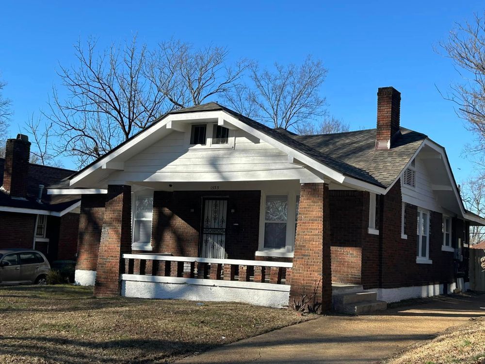 A small brick house with a porch and a car parked in front of it