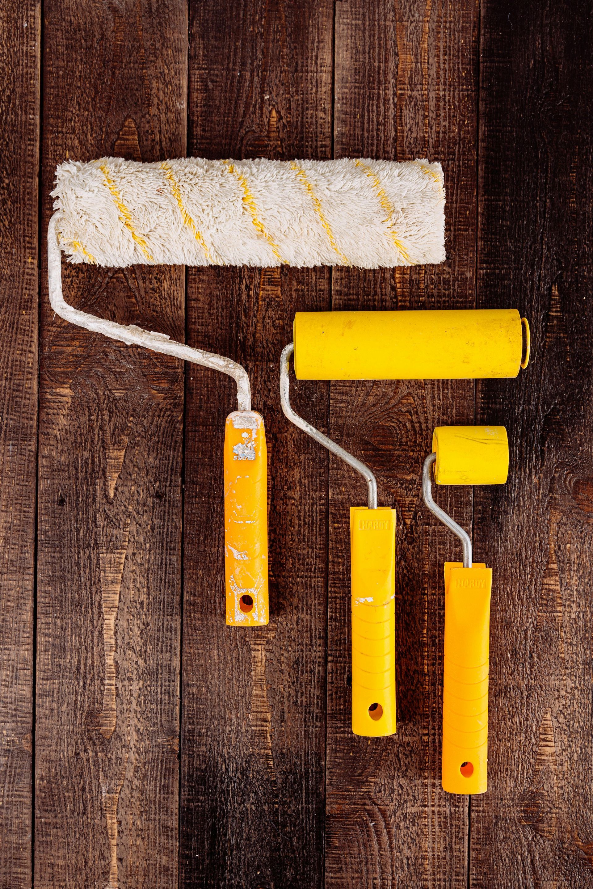 Three paint rollers with yellow handles are sitting on a wooden table.