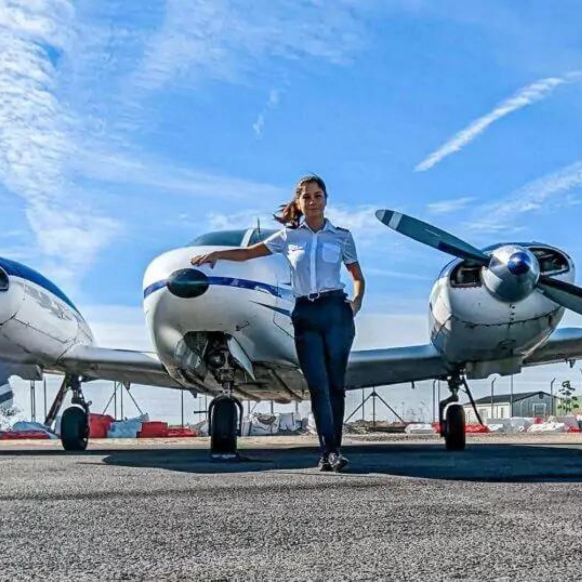 A woman is standing in front of two small planes on a runway.