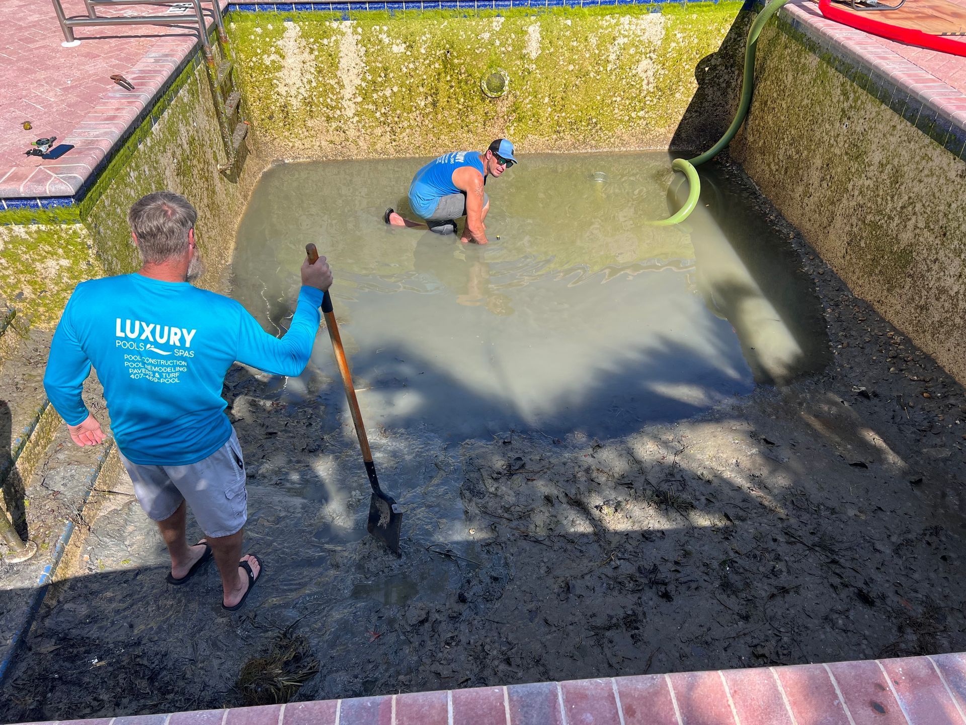 Two men are working on a swimming pool with a shovel.