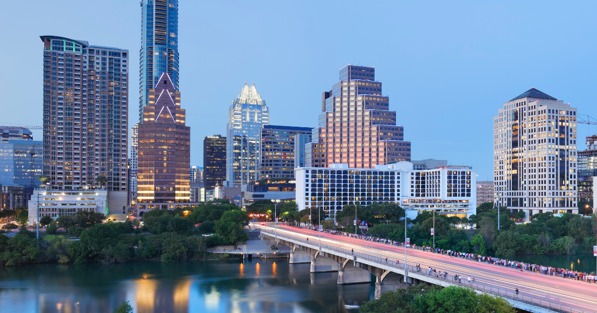 Austin, Texas skyline at dusk, with buildings of various heights and a bridge over a river.