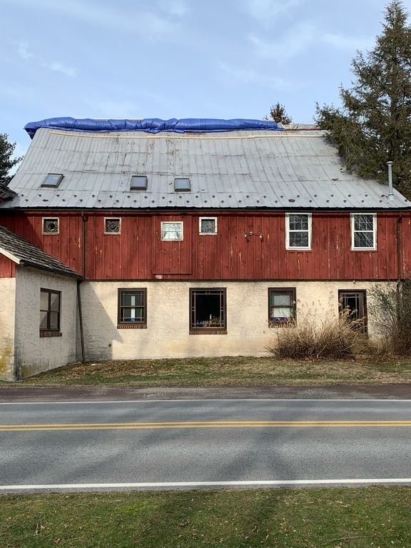 A red barn with a blue tarp on the roof is next to a road.