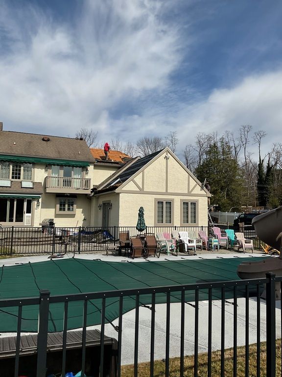 A fence surrounds a swimming pool with a house in the background.