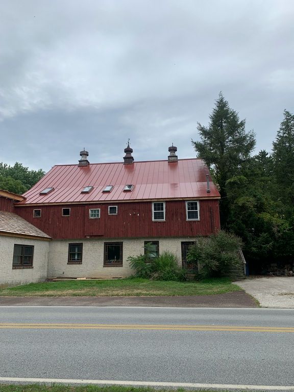 A red barn with a metal roof is next to a road.